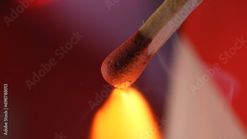 Macro shot of a burning match against a red studio background. The flame of the burning match illuminates the dark space. The burning match is enveloped in an orange, vibrant and dynamic flame. photo