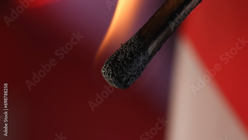 Macro shot of a burning match against a red studio background. The flame of the burning match illuminates the dark space. The burning match is enveloped in an orange flame.