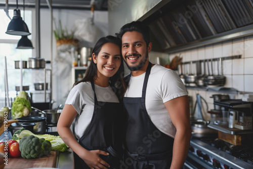 Smiling young hispanic couple posing at their restaurant kitchen	 photo