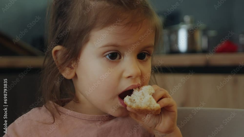 Happy cute little girl enjoying eating bread at breakfast in kitchen at home. Little girl sitting at a kitchen table early in the morning and having breakfast Happy cute little girl enjoying eating bread at breakfast in kitchen at home. Little girl sitting at a kitchen table early in the morning and having breakfast