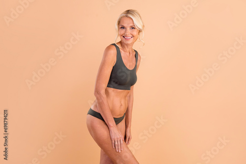 Photo of young happy woman demonstrates strong nice body sporty shape perfect ideal skin empty space isolated on beige color background