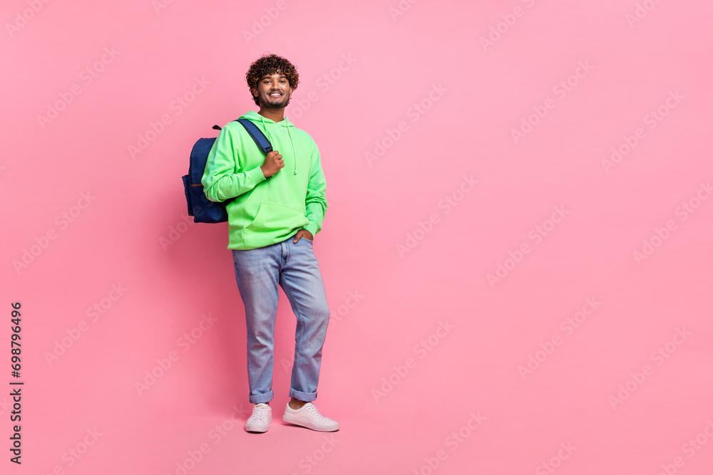 Full body photo of optimistic student wavy haired guy wearing green hoodie with jeans bring rucksack isolated on pink color background Full body photo of optimistic student wavy haired guy wearing green hoodie with jeans bring rucksack isolated on pink color background
