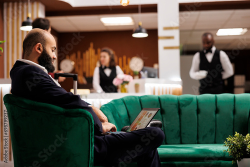 Middle eastern man using laptop in lobby, sitting in lounge area and preparing speech for international business meeting. Professional employee travelling for work, hotel reception.