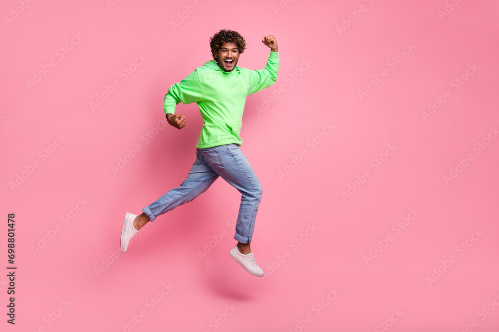 Full length photo of successful crazy arab guy wearing green sweatshirt jeans white sneakers jumping isolated on pink color background