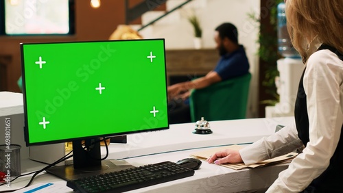 Hotel staff working with pc greenscreen at reception, talking to tourists upon their arrival. Front desk worker using blank copyspace template with isolated display, doing check in. Tripod shot.