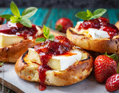 closeup of freshly baked bread buns with melted brie cheese and strawberry jam topping photo