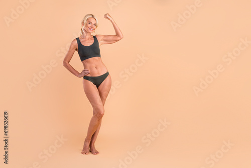 Full length photo of strong woman showing muscular arm biceps triceps sport gym training empty space isolated on beige color background