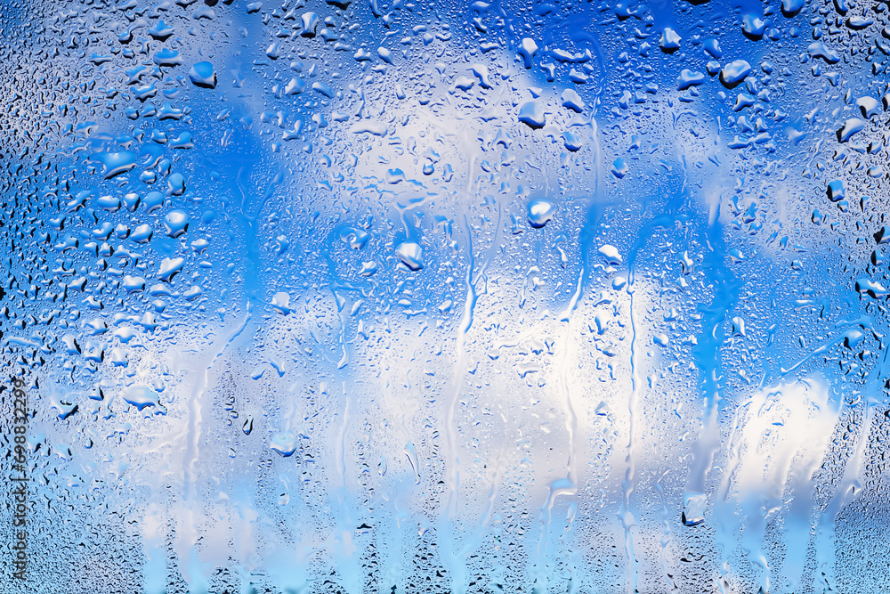 Raindrops on the window. Water drops on glass. Abstract background. Blue sky with clouds. Texture of drops