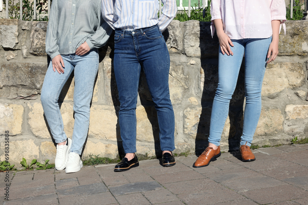 Women in stylish jeans near stone wall outdoors on sunny day, closeup Women in stylish jeans near stone wall outdoors on sunny day, closeup