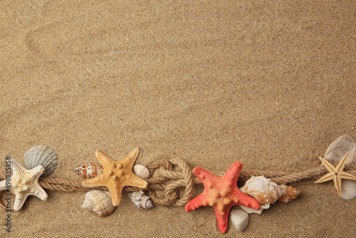 Beautiful sea stars, shells and ropes on sand, flat lay. Space for text