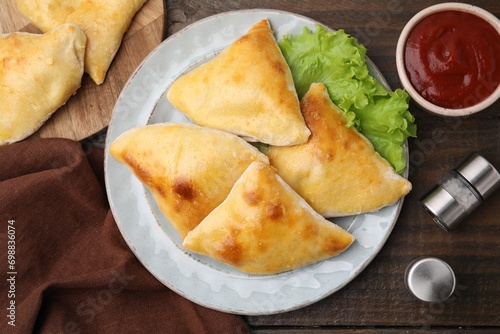 Delicious samosas with lettuce and tomato sauce on wooden table, flat lay