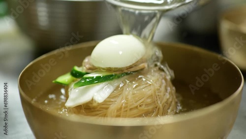 국수가 담겨진 냉면 그릇에 시원한 육수를 부어 넣는 