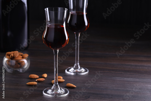 Liqueur glasses with tasty amaretto and almonds on wooden table, space for text