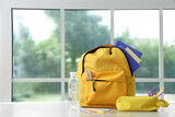 Yellow school backpack with stationery and bottle of water on wooden table near window in classroom