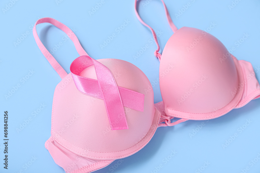 Bra with pink ribbon on blue background, closeup. Breast cancer awareness concept