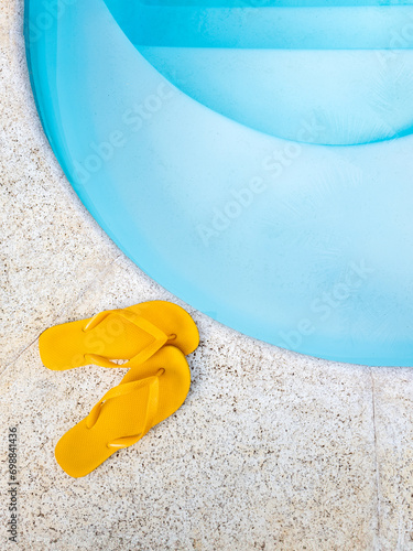 um par de chinelos amarelos perto da borda da piscina, a piscina é de azul claro e tem água cristalina. photo