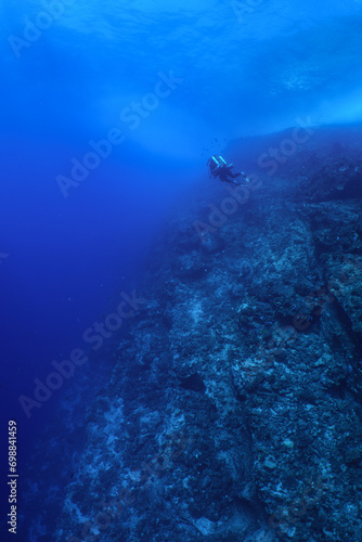 Scuba diver swim along a tropical wall near Maui, wearing a closed circuit rebreather. A rocky reef grows on the back wall at molokini crater.