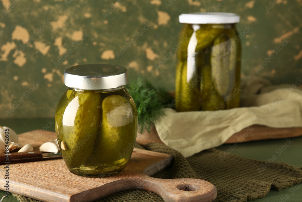 Jars with tasty canned cucumbers on table near green wall Jars with tasty canned cucumbers on table near green wall