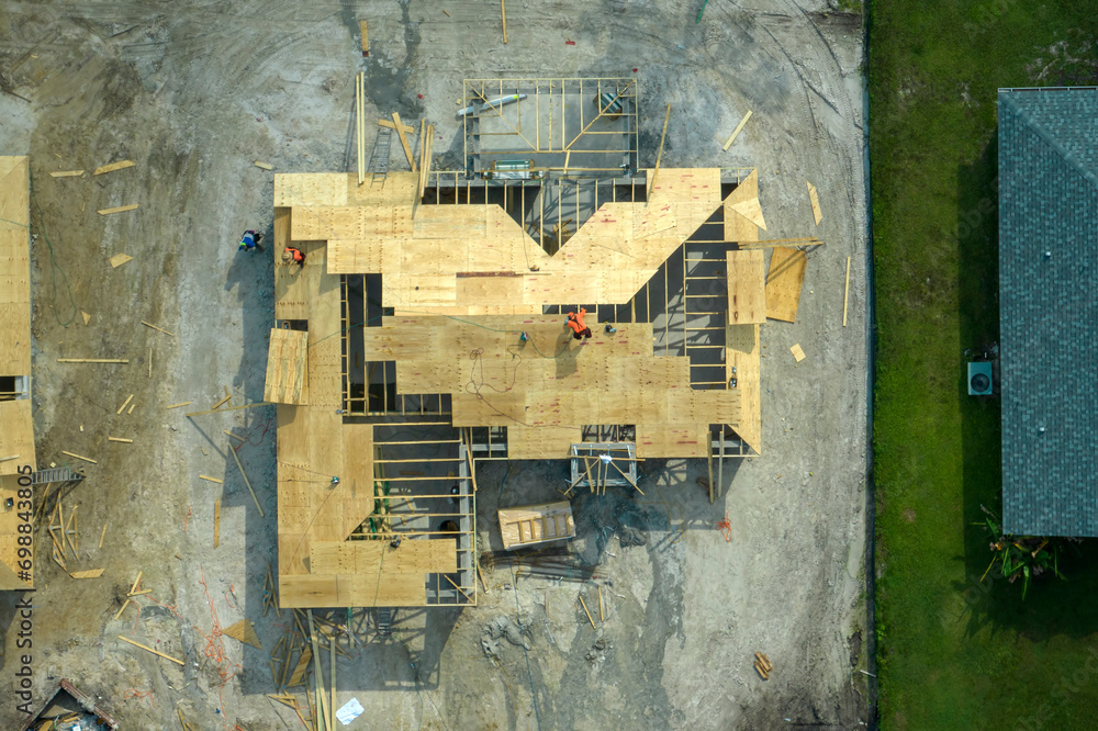 Fototapeta premium Professional builders working on roof construction of unfinished suburban home with wooden frame structure in Florida rural area. Concept of housing development in America