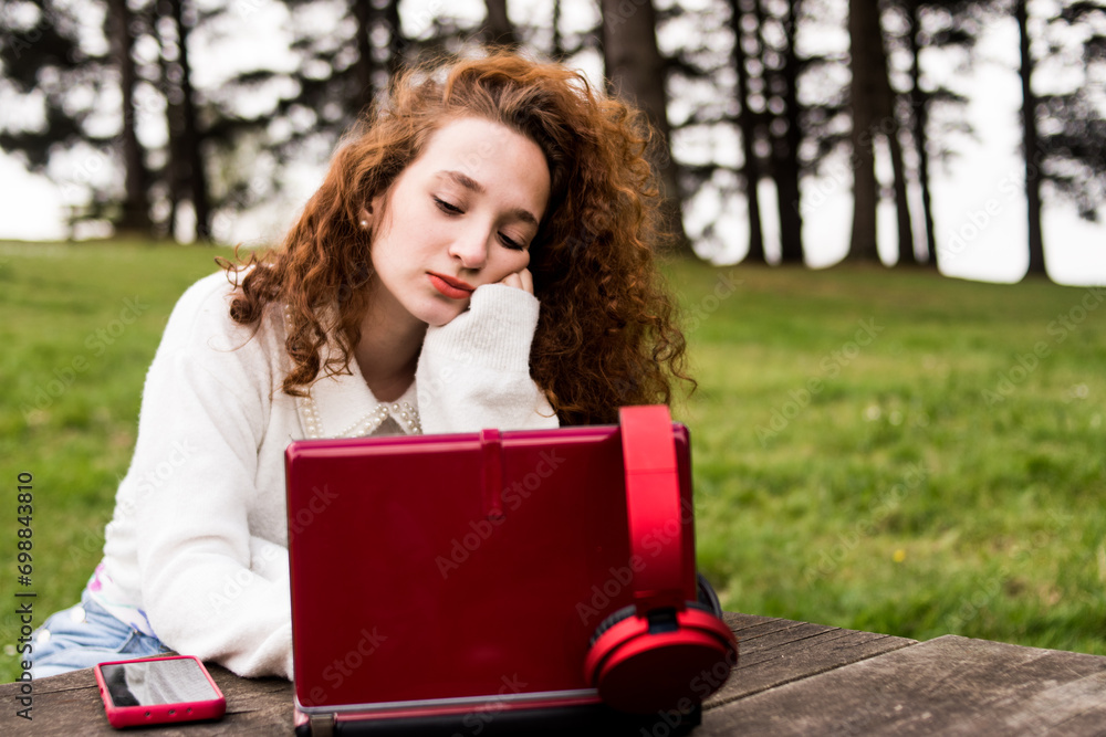 Redhead woman studying outdoors with her computer and mobile phone Redhead woman studying outdoors with her computer and mobile phone