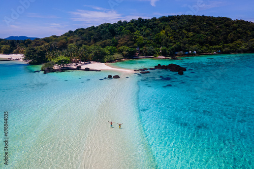 couple walking at the beach of Koh Kham Trat Thailand, aerial view of the tropical island near Koh Mak Thailand with a white sandy beach with palm trees and big black boulder stones in the ocean