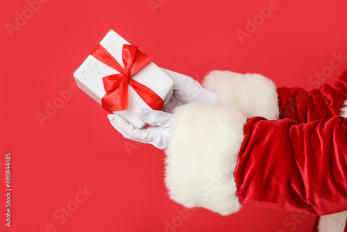 Santa Claus holding gift box on red background, closeup