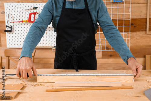 Mature carpenter measuring wooden plank at table in shop