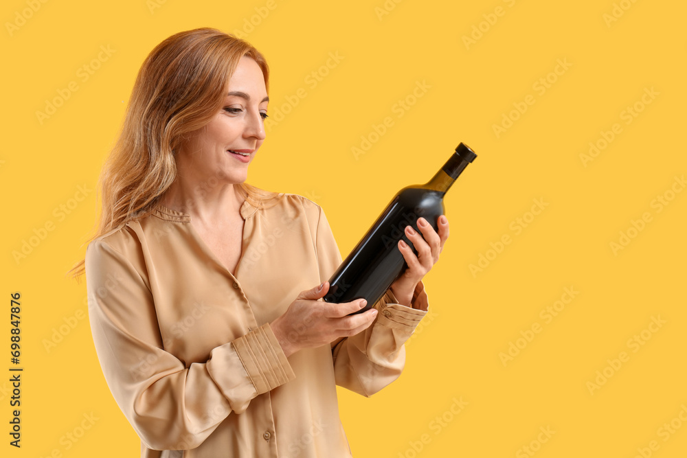 Mature woman with bottle of wine on yellow background Mature woman with bottle of wine on yellow background