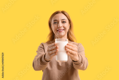 Mature woman with glass of milk on yellow background
