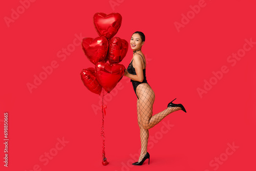 Beautiful young happy Asian woman in sexy underwear with heart-shaped balloons on red background. Valentine's Day celebration