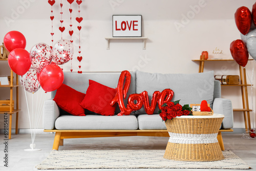 Interior of festive room with grey sofa, word LOVE made from balloons and bouquet of roses on coffee table. Valentine's Day celebration #698854474