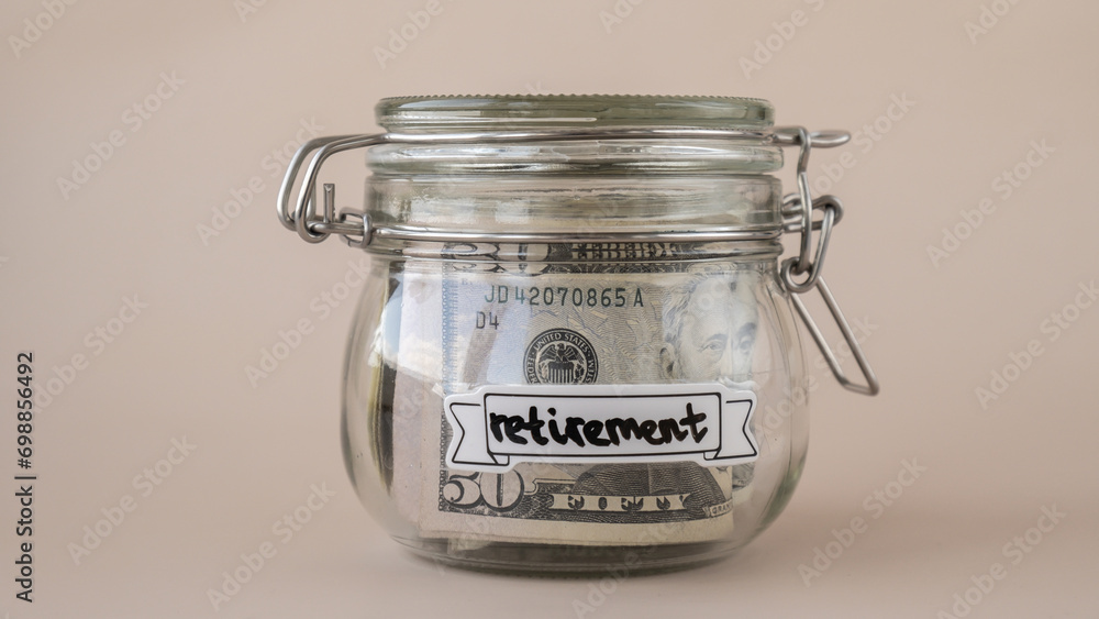 Saving Money In Glass Jar filled with Dollars banknotes. RETIREMENT transcription in front of jar. Managing personal finances extra income for future insecurity. Beige background Saving Money In Glass Jar filled with Dollars banknotes. RETIREMENT transcription in front of jar. Managing personal finances extra income for future insecurity. Beige background