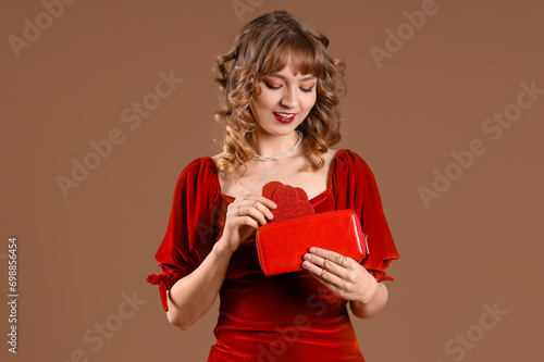 Beautiful young woman with wallet and hearts on brown background. Valentine's Day celebration
