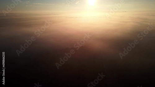 Drone flies high above and captures dense fog over land and beautiful sunset