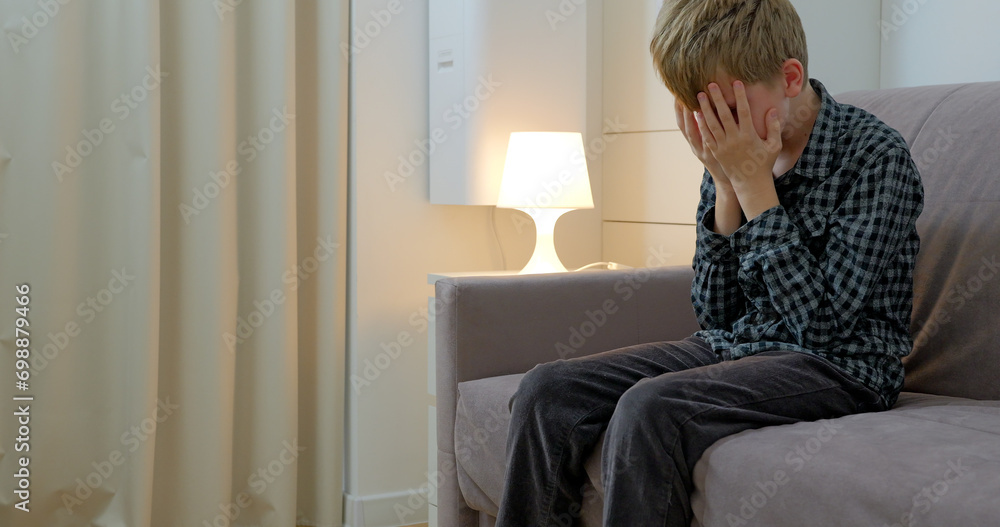 Boy is suffering from a headache sitting on sofa at home Boy is suffering from a headache sitting on sofa at home