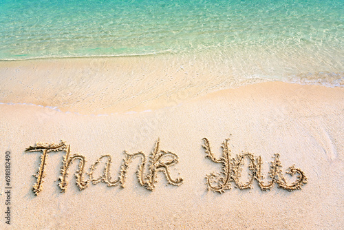 Thank you lettering on the beach with wave and clear blue sea. Thank you card with message written in golden sand on clean beach background. Gratitude concept. Copy space.