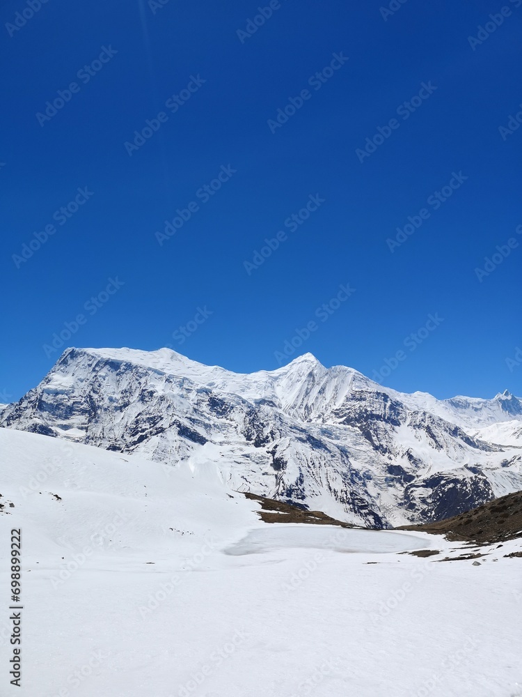A majestic mountain dressed in a white blanket of snow, standing tall beneath a flawless and radiant blue sky.