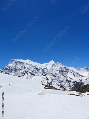 A majestic mountain dressed in a white blanket of snow, standing tall beneath a flawless and radiant blue sky.