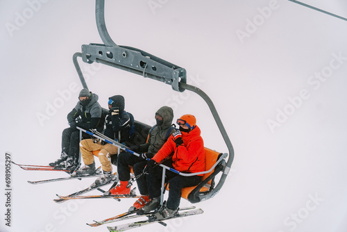 Tourists in ski suits and goggles ride a chairlift up a foggy mountain
