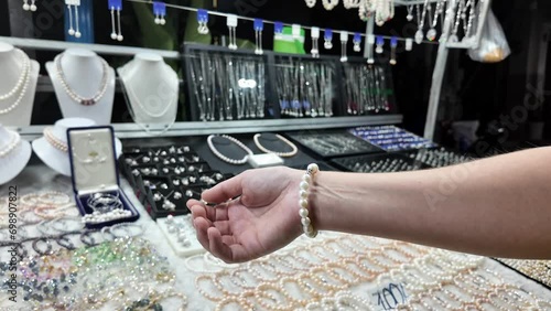 Customer trying on a white pearl bracelet at a jewelry store, with various necklaces and earrings displayed in the background photo