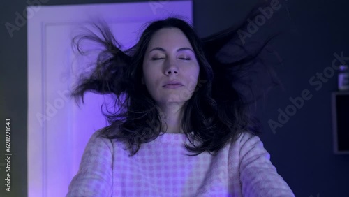 Portrait of a young sleepwalking woman in pajamas slowly raising her hands in front of her at night in a room. Her hair is flying in the air. The concept of somnambulism photo