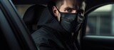 A man in a black car wears a medical mask for protection during the coronavirus epidemic.