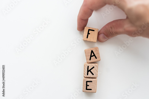 The word FAKE, spelt with wooden letter tiles, over a white background.