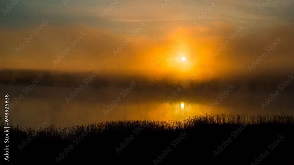 the sun rising over the surface of a lake shrouded in fog