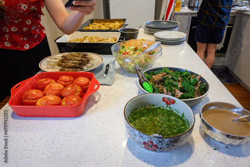 Woman holding a smartphone taking photos of festival food on the kitchen benchtop. Home cooking and entertainment concept.