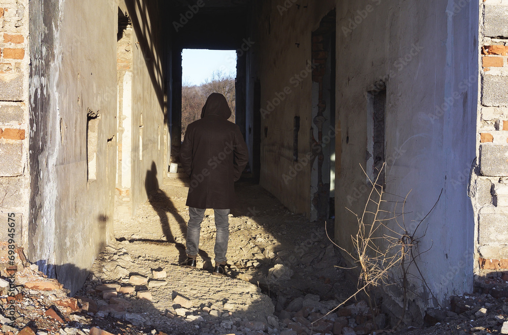 A man dressed in a hooded coat in the hallway of a ruined building.