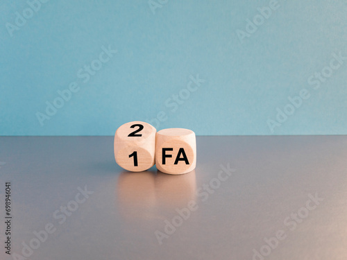 Turned wooden a cube and changes the abbreviation 1FA (One factor authentication) to 2FA (Two factor authentication). Beautiful blue background, grey table. Copy space photo