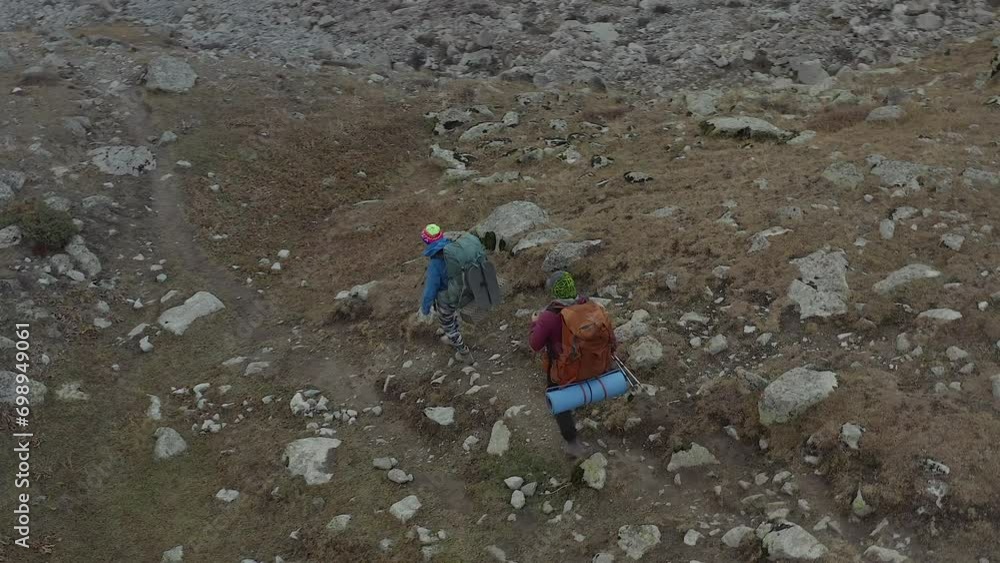 Young people in colorful clothes with large backpacks and trekking poles are walking along a narrow rocky mountain path. Active recreation in the mountains. Ala-Archa National Park in Kyrgyzstan. Young people in colorful clothes with large backpacks and trekking poles are walking along a narrow rocky mountain path. Active recreation in the mountains. Ala-Archa National Park in Kyrgyzstan.