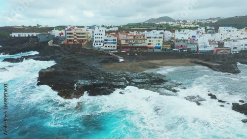 Aerial view in orbit over the beach and houses on the coast of El Puertillo in the north of the island of Gran Canaria and with large waves hitting the coast. photo