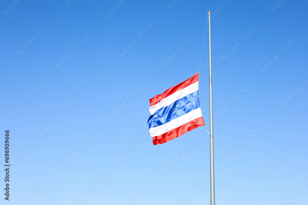 Thai flag was lowered to half-mast. Lowering of flag on metal pole on blue sky background with copy space and selective focus.
